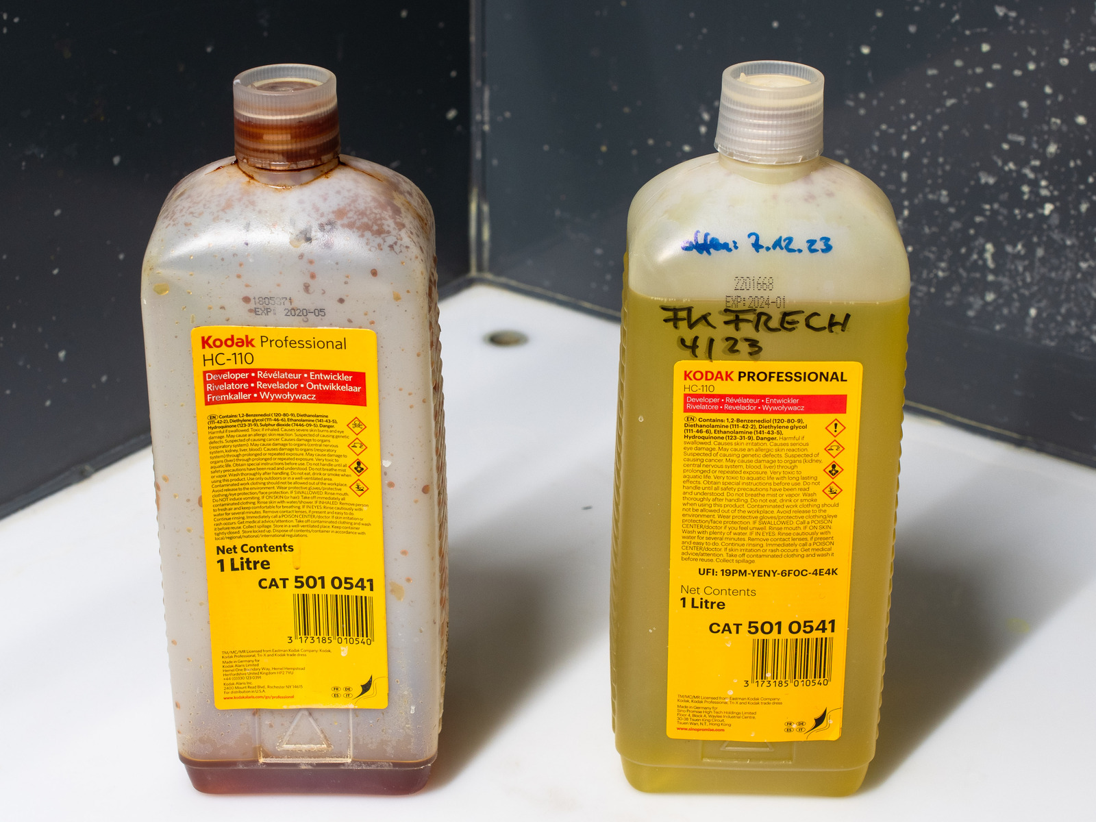 Zwei 1-Liter-Flaschen Kodak-Entwicklerkonzentrat HC-110 (CAT 501 0541) im Laborbecken. Die linke Flasche ist beinahe leer, die Restflüssigkeit ist dunkelbraun; die rechte Flasche ist voll, die Flüssigkeit ist dunkelgelb. Die rechte Flasche ist handschriftlich beschriftet: Fk Frech 4/23 offen: 7.12.23