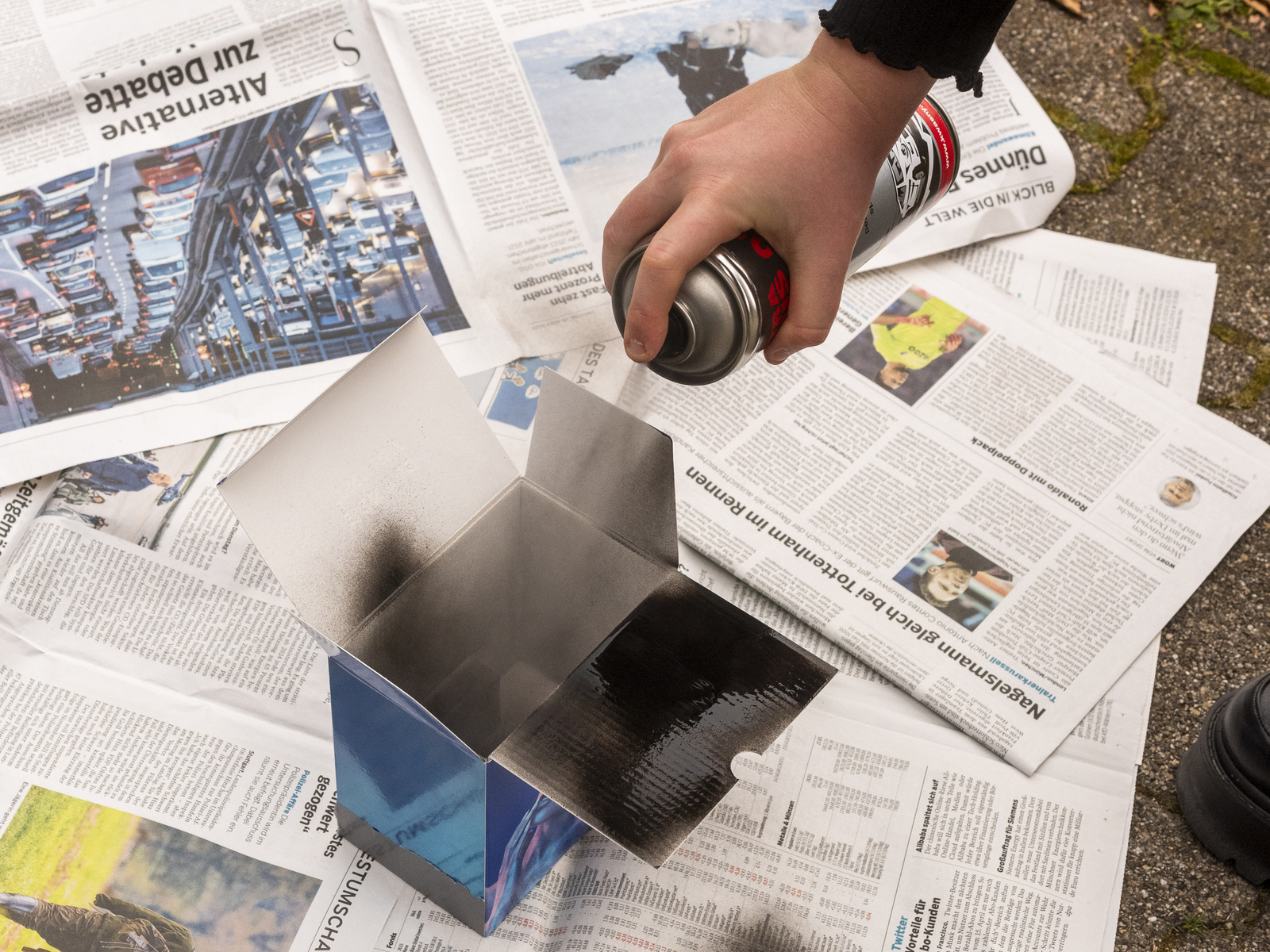 Farbbild (born-digital): Das Innere einer Pappschachtel wird mit Sprühlack geschwärzt (Foto: © Martin Frech 11/2024)